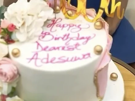 A birthday cake decorated with white and pink flowers, a gold 60th topper and a birthday message, at Alali in Lagos
