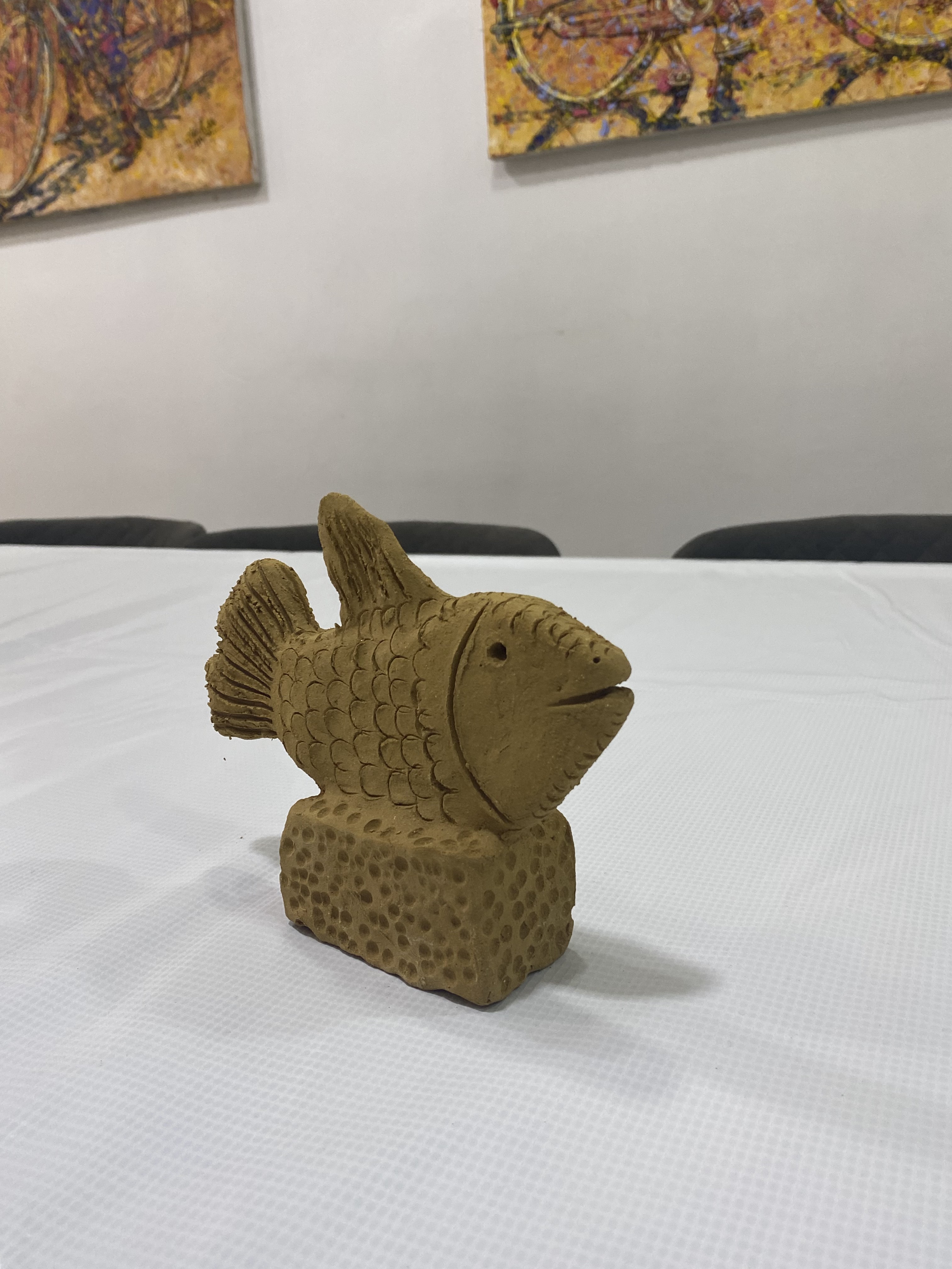 A clay fish sculpture with carved scales on a textured base at Alali