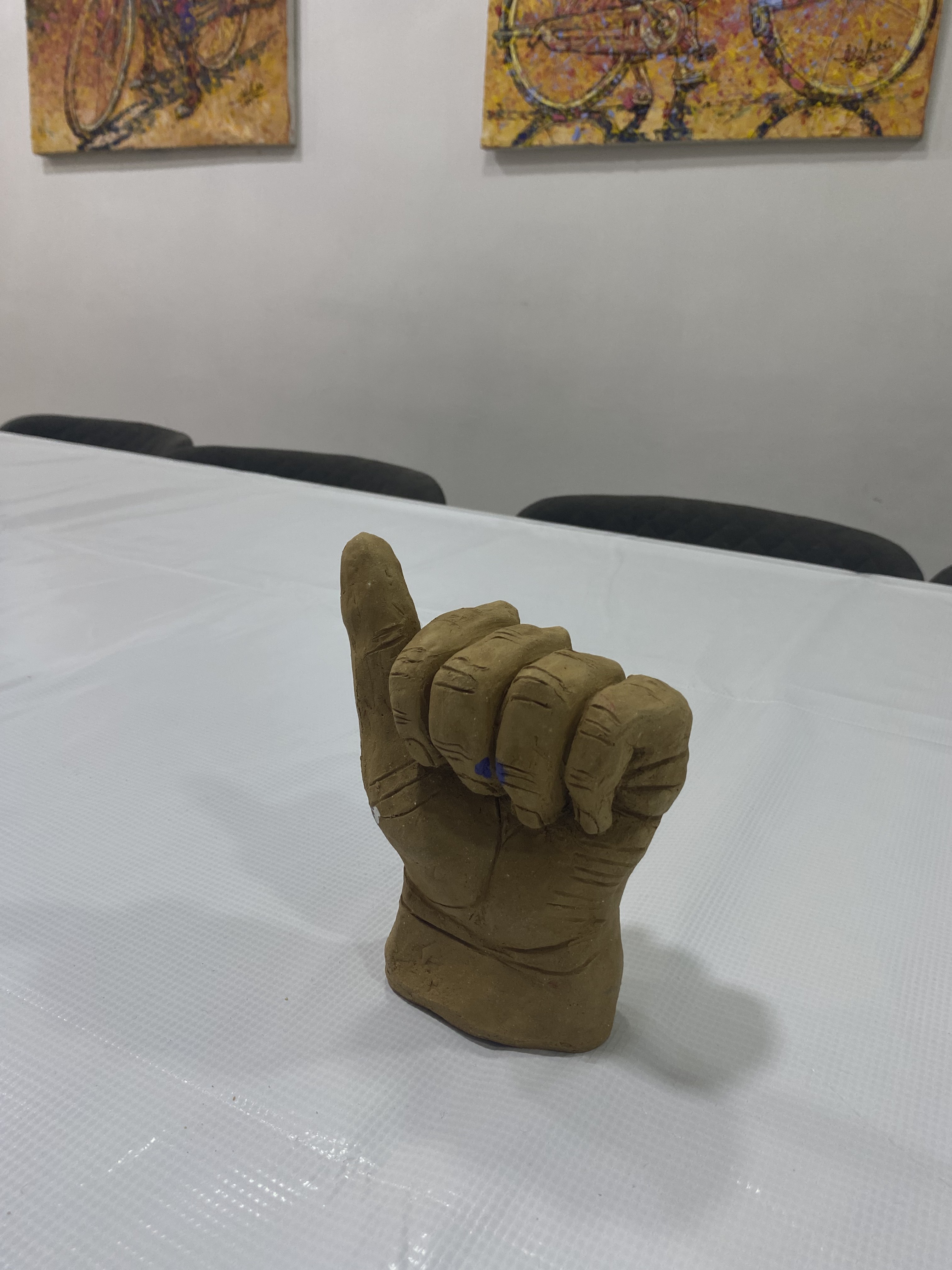 A clay hand sculpture with curled fingers and a raised thumb at Alali